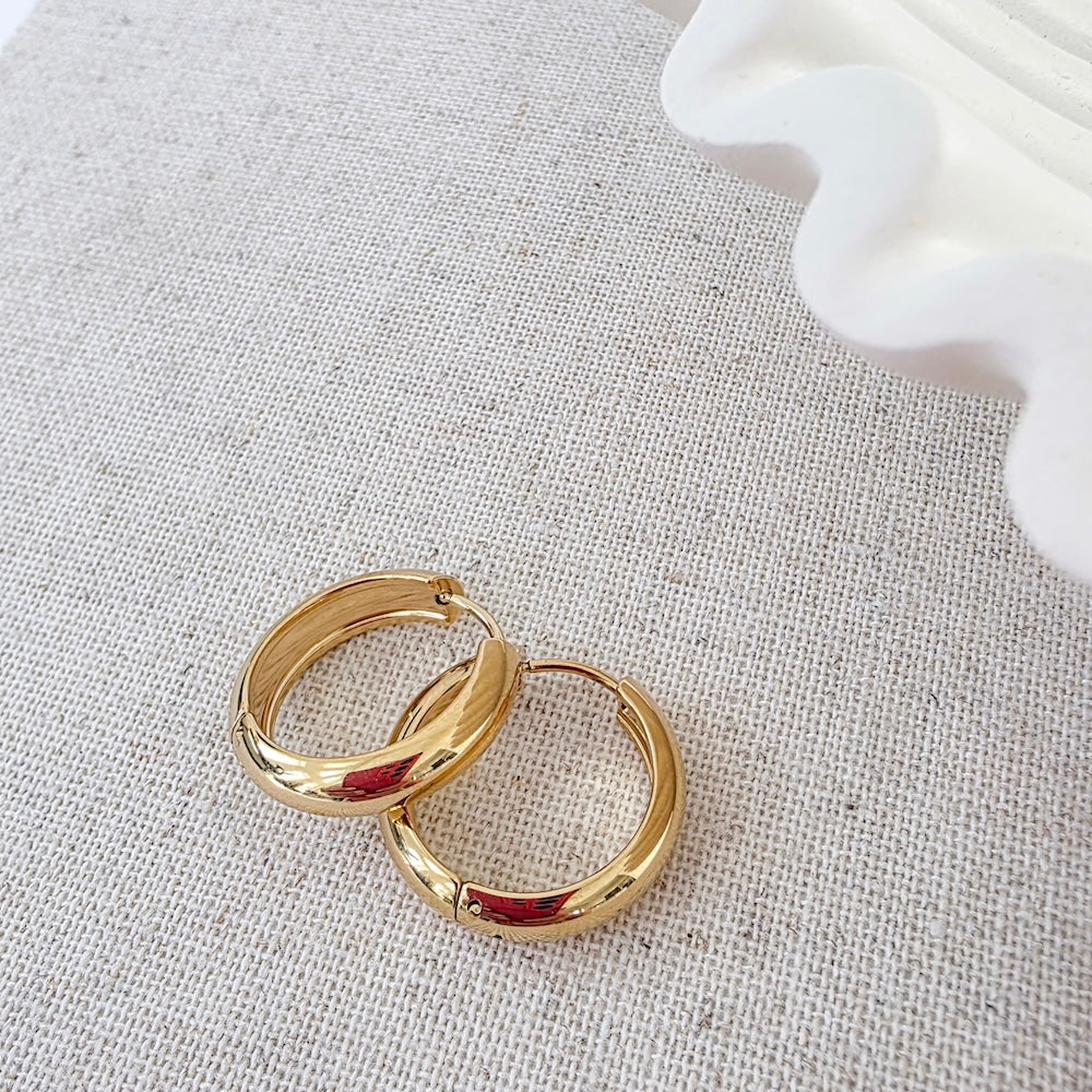 Pair of gold hoop earrings on light fabric, with red enamel in the hoops
