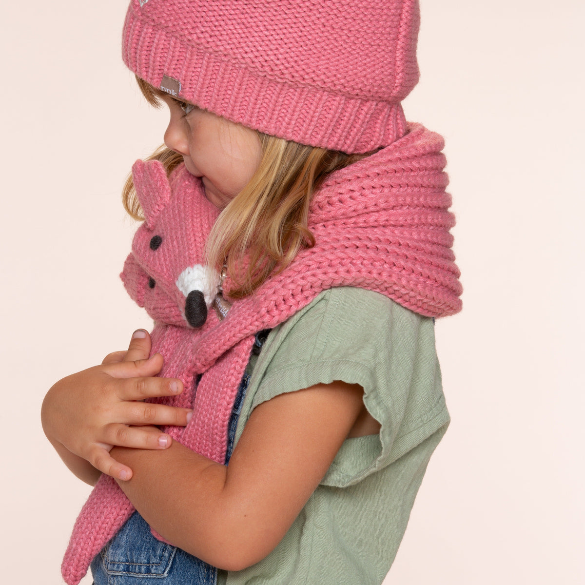 Side view of a child wearing a pink knitted fox scarf, showing its face and long hanging ends.