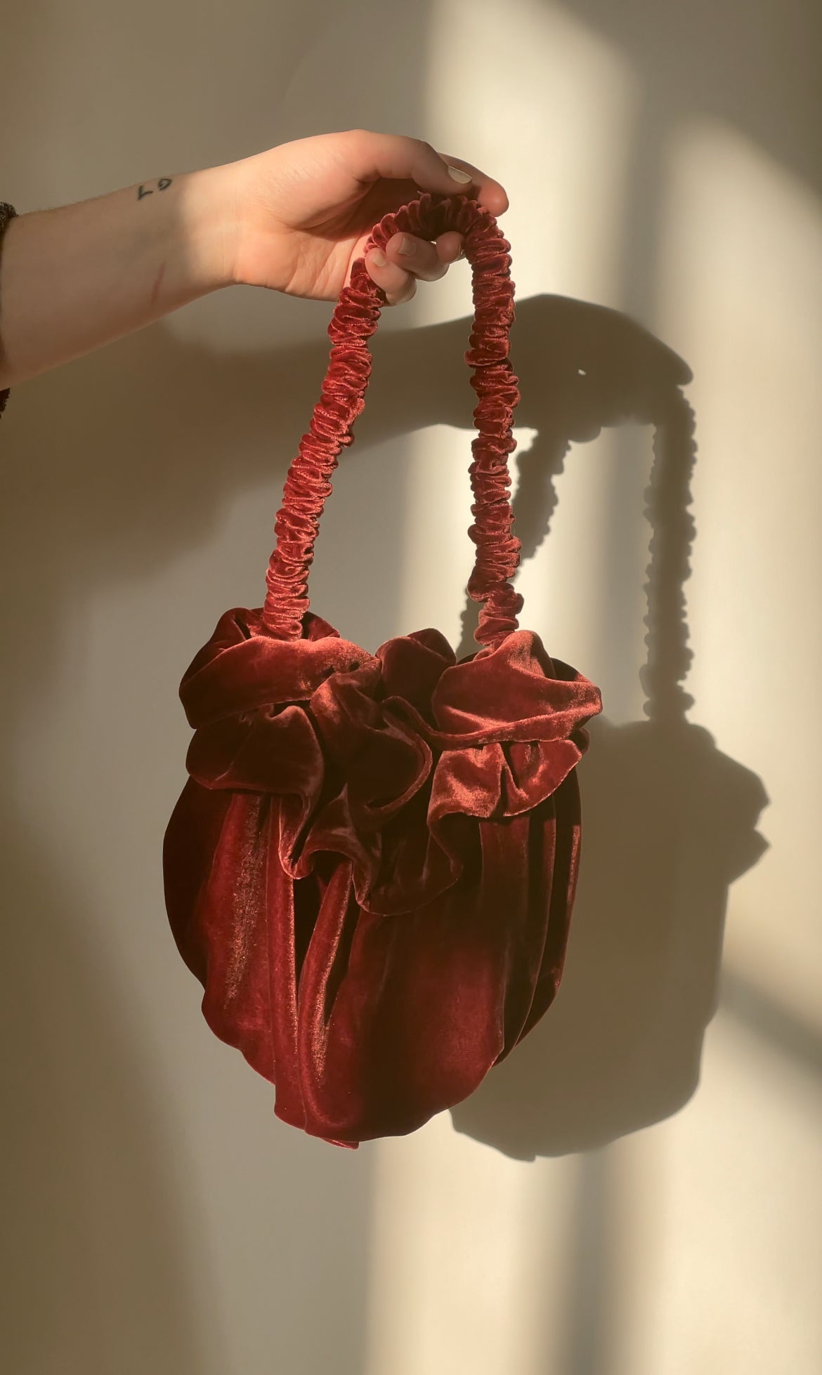 Crimson velvet Bloom bag held by its gathered handle
