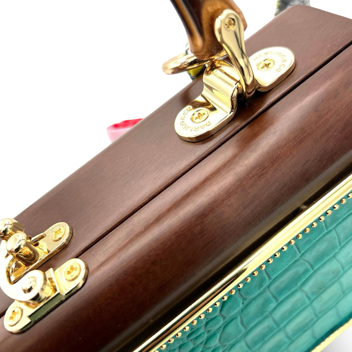 Gator Glam Bag detail showing polished wood frame, gold handle fittings, and teal embossed panel