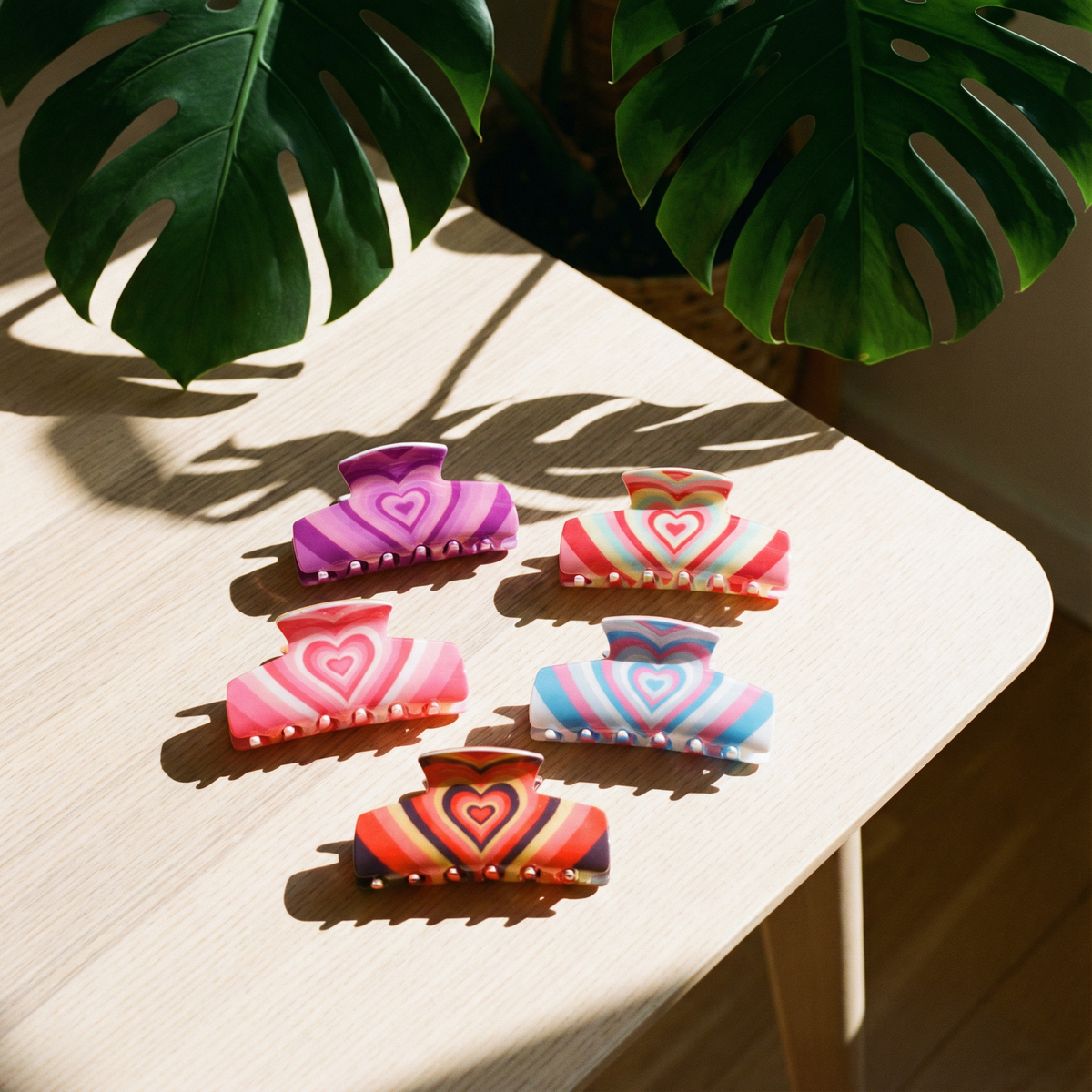 Five colorful heart-pattern hair claw clips arranged on a wooden table