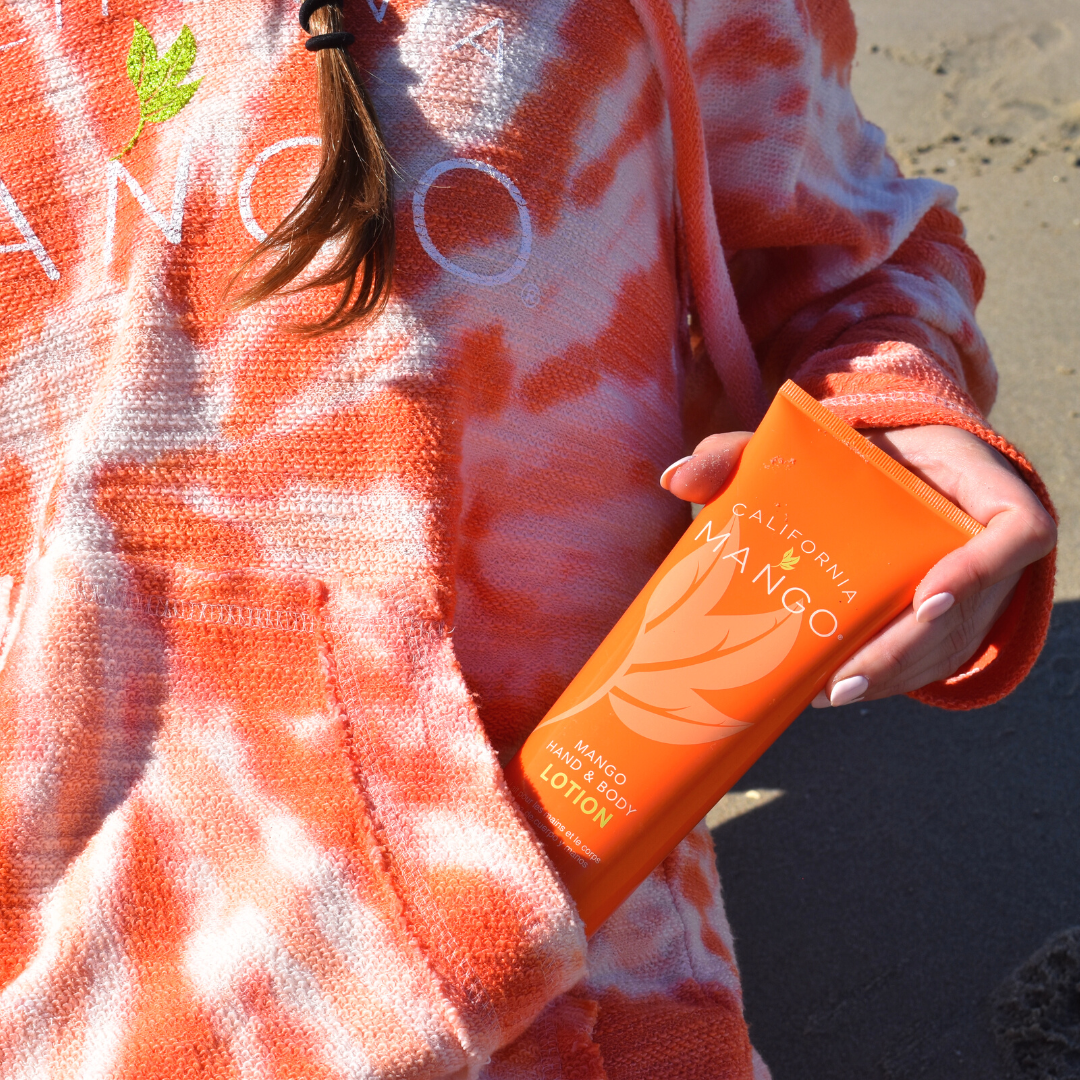 Orange lotion tube with green cap held in hand, California Mango
