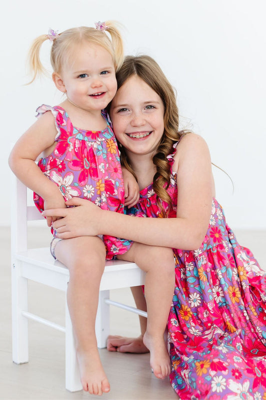Pink floral ruffle cross-back romper worn by child with elastic leg openings