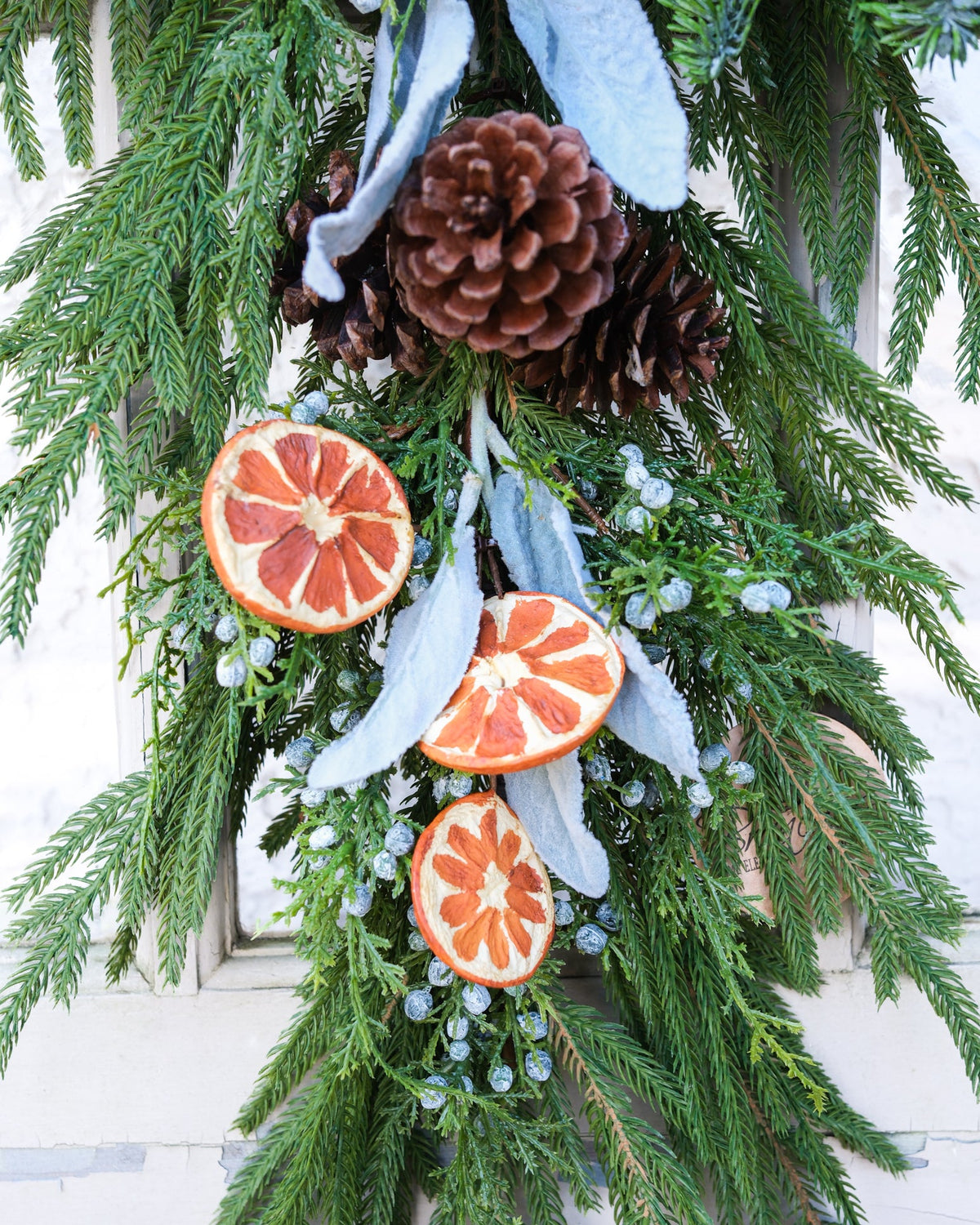 Evergreen garland close-up with pinecones and orange slice ornaments over white ribbon tails