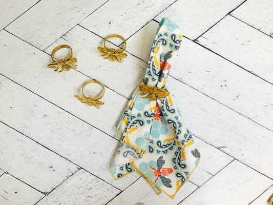 Bee-pattern cloth napkin set of four, light blue with gray and orange accents, folded with ties