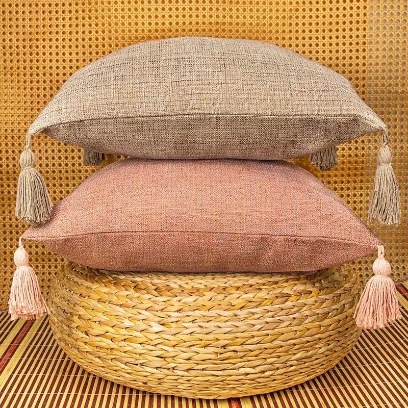 Taupe and dusty pink pillow covers with fringe tassel trim on a woven basket