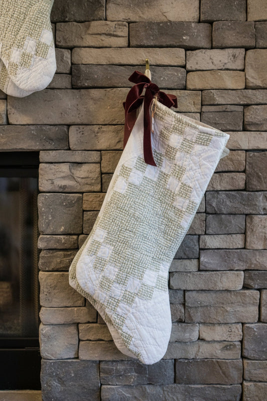 Quilted stocking with patchwork squares and dark ribbon bow, hanging on a wall.