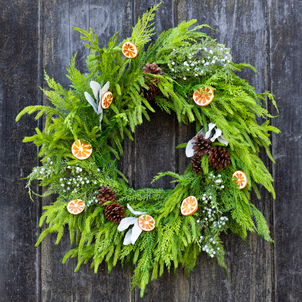 Evergreen wreath with orange slice ornaments, pinecones, white blossoms, and berry clusters