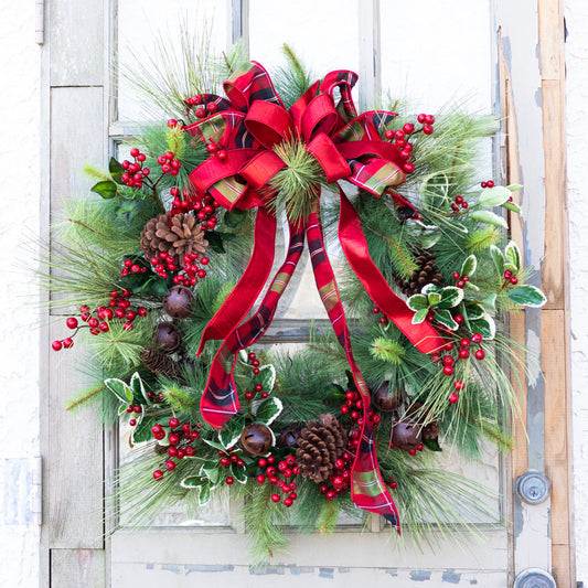 Holiday wreath with red ribbon bow, pine branches, pinecones, red berries, and small bells