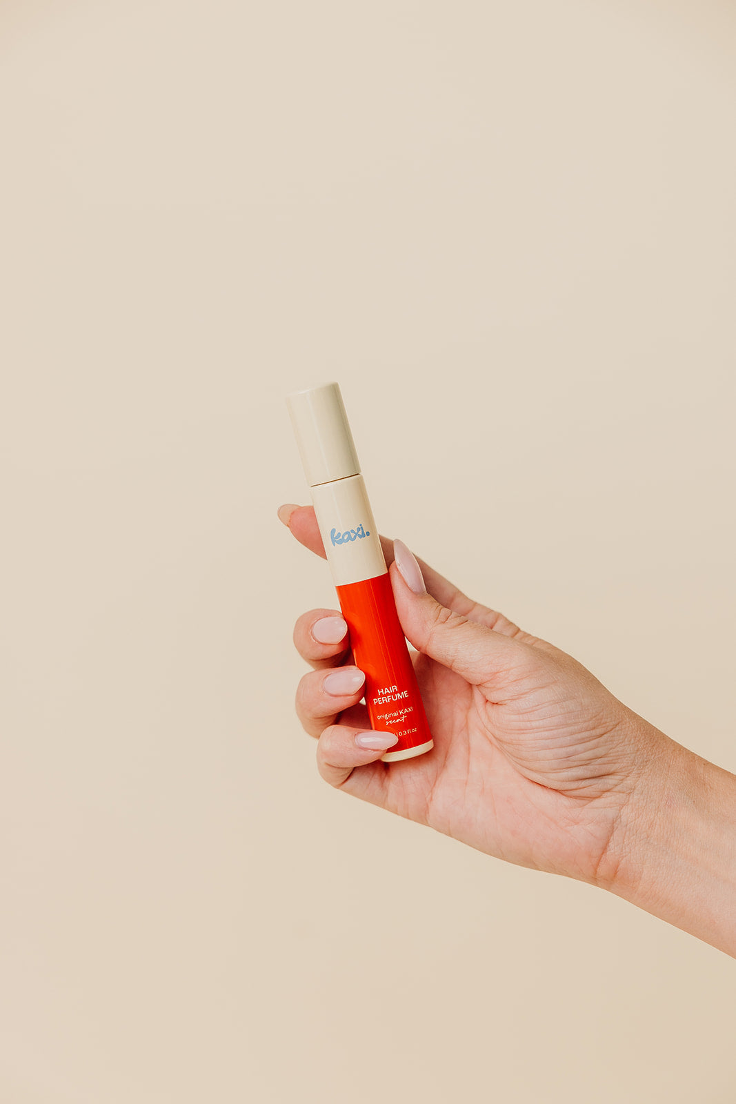 Hand holding hair perfume spray bottle with red label and cream cap
