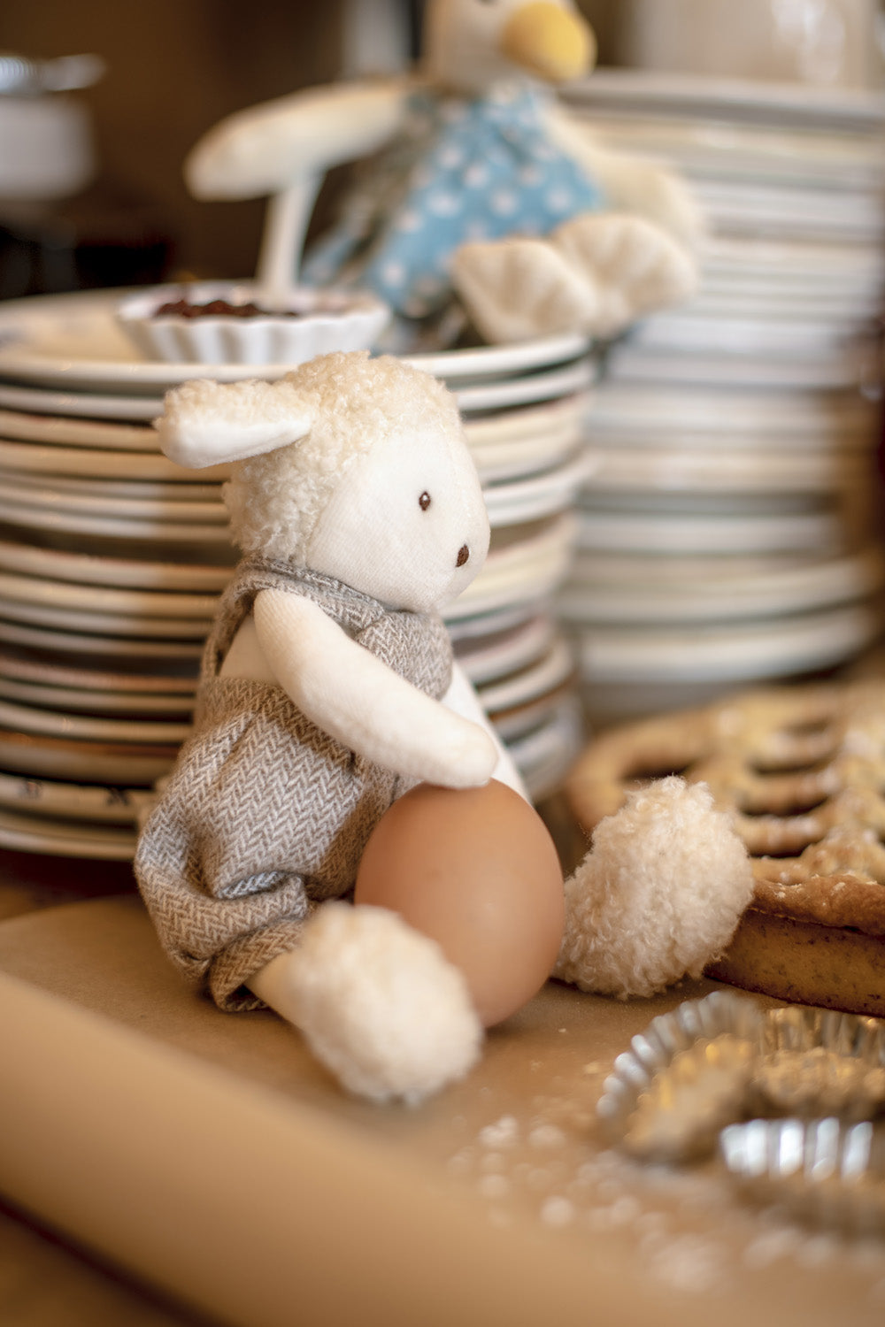 Small stuffed sheep toy sitting with gray overalls and beige hooves