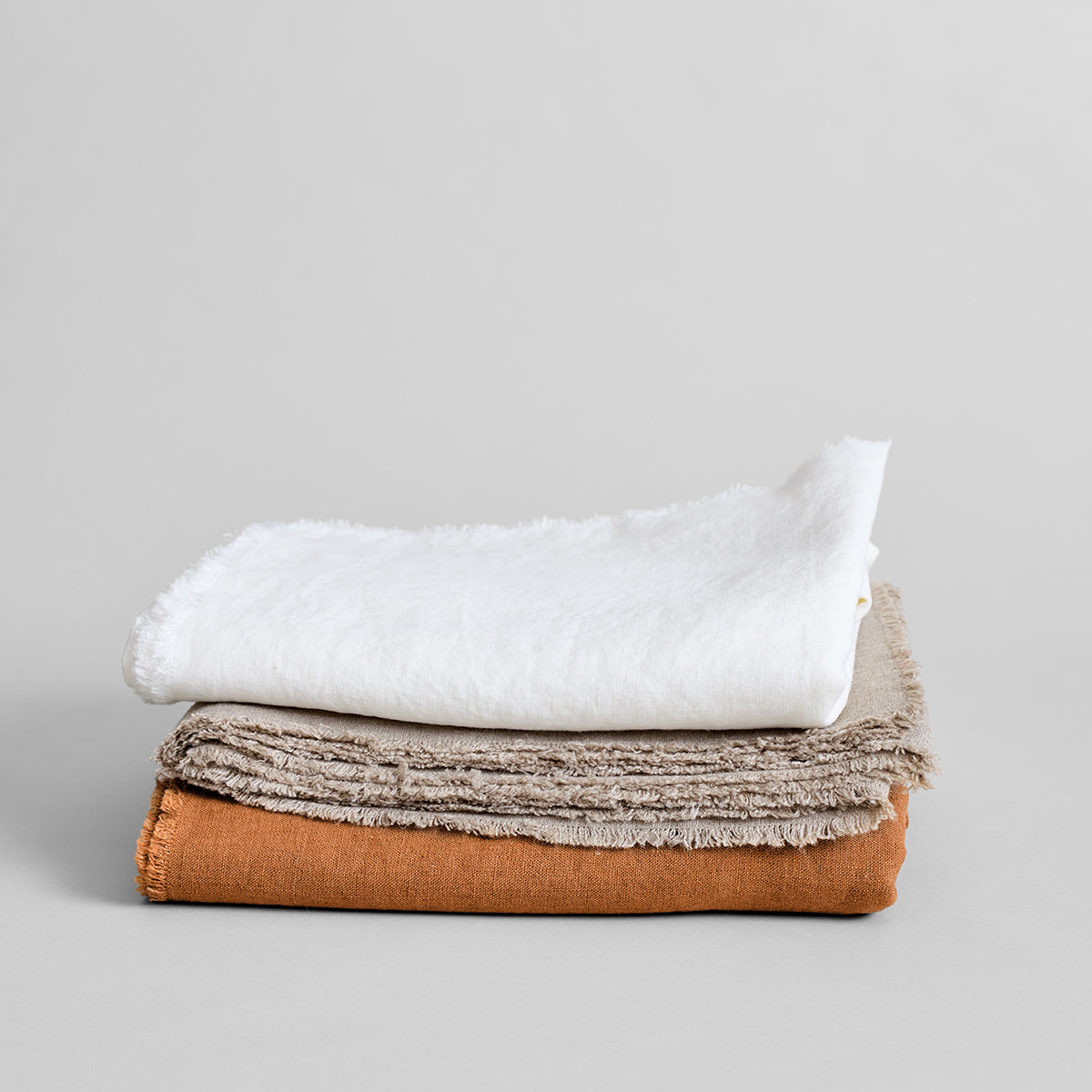 Fringed linen tablecloth stack in white, gray, and rust colors folded together