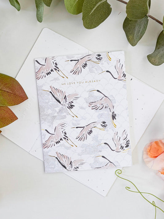 Seeded baby congratulations card on top of blank envelopes, feather pattern in pink and black