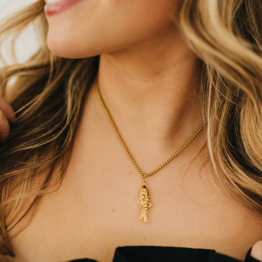 Gold-tone lucky fish pendant on fine chain necklace, close-up at the collar