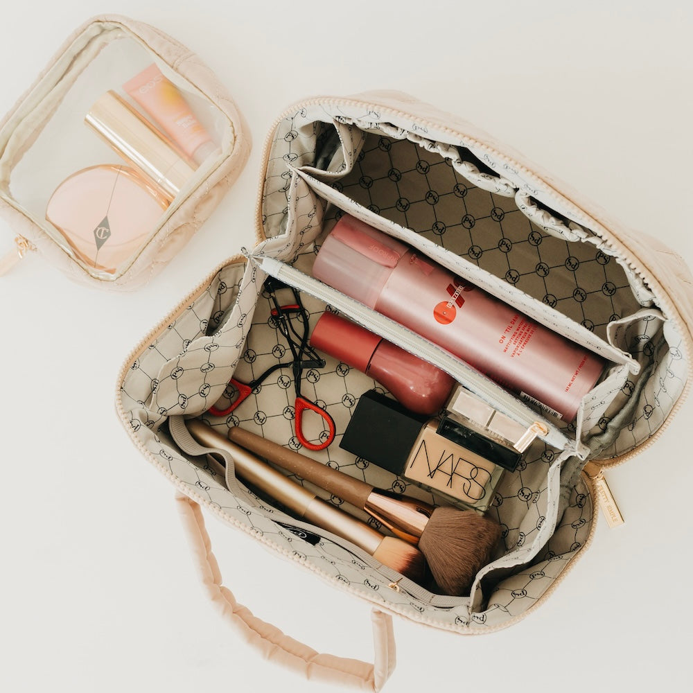 Taupe quilted cosmetics bag open with interior pockets and pink makeup items inside.