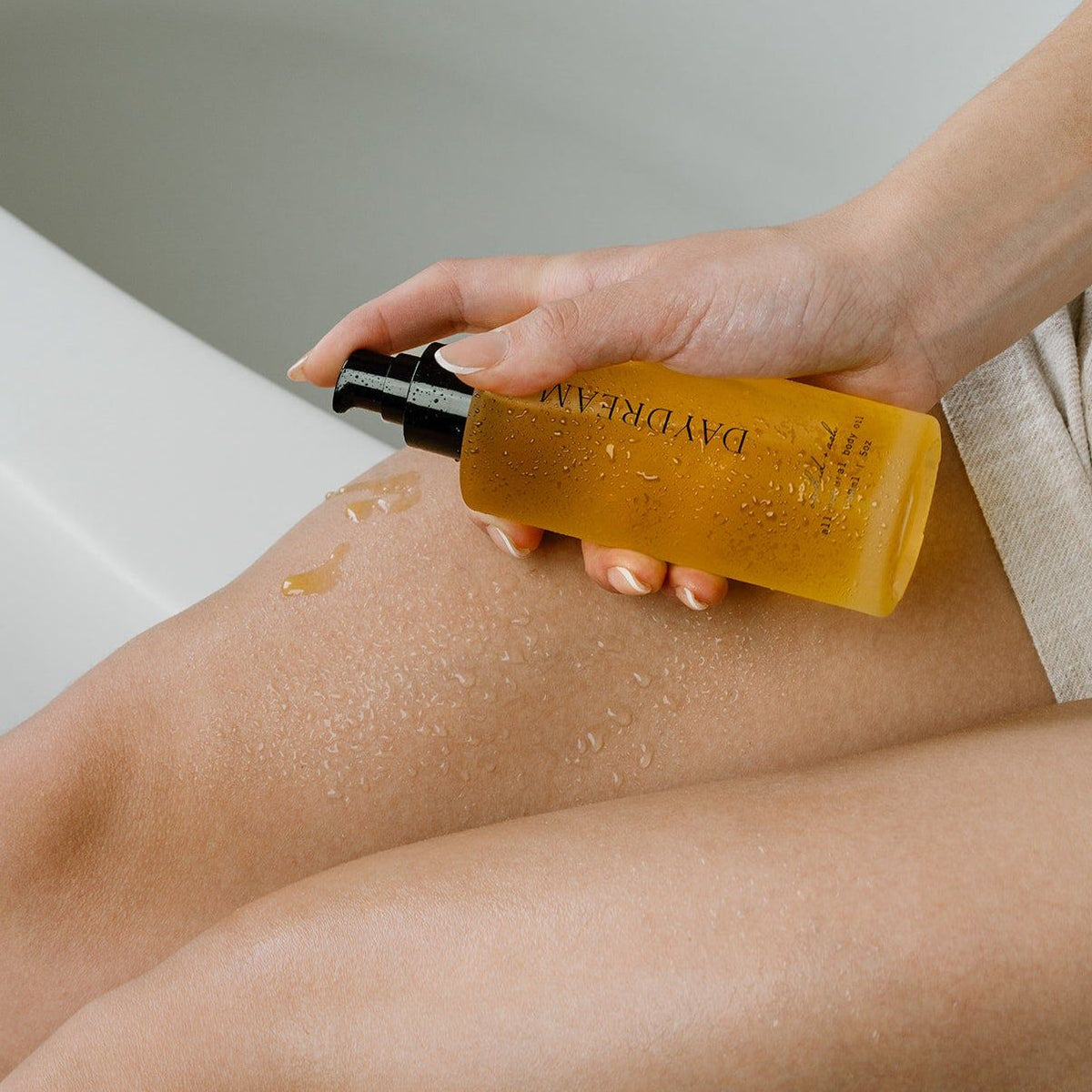 Amber body oil dispensed onto bare skin from black pump bottle.
