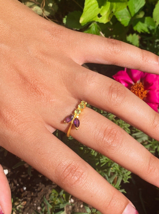 Gold vine ring on hand with green peridot stones and a purple amethyst marquise center
