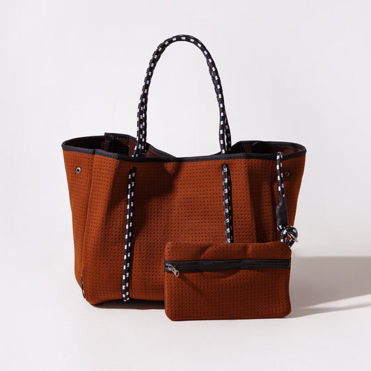 Rust-brown perforated tote with black lining, patterned handles, front zip pouch