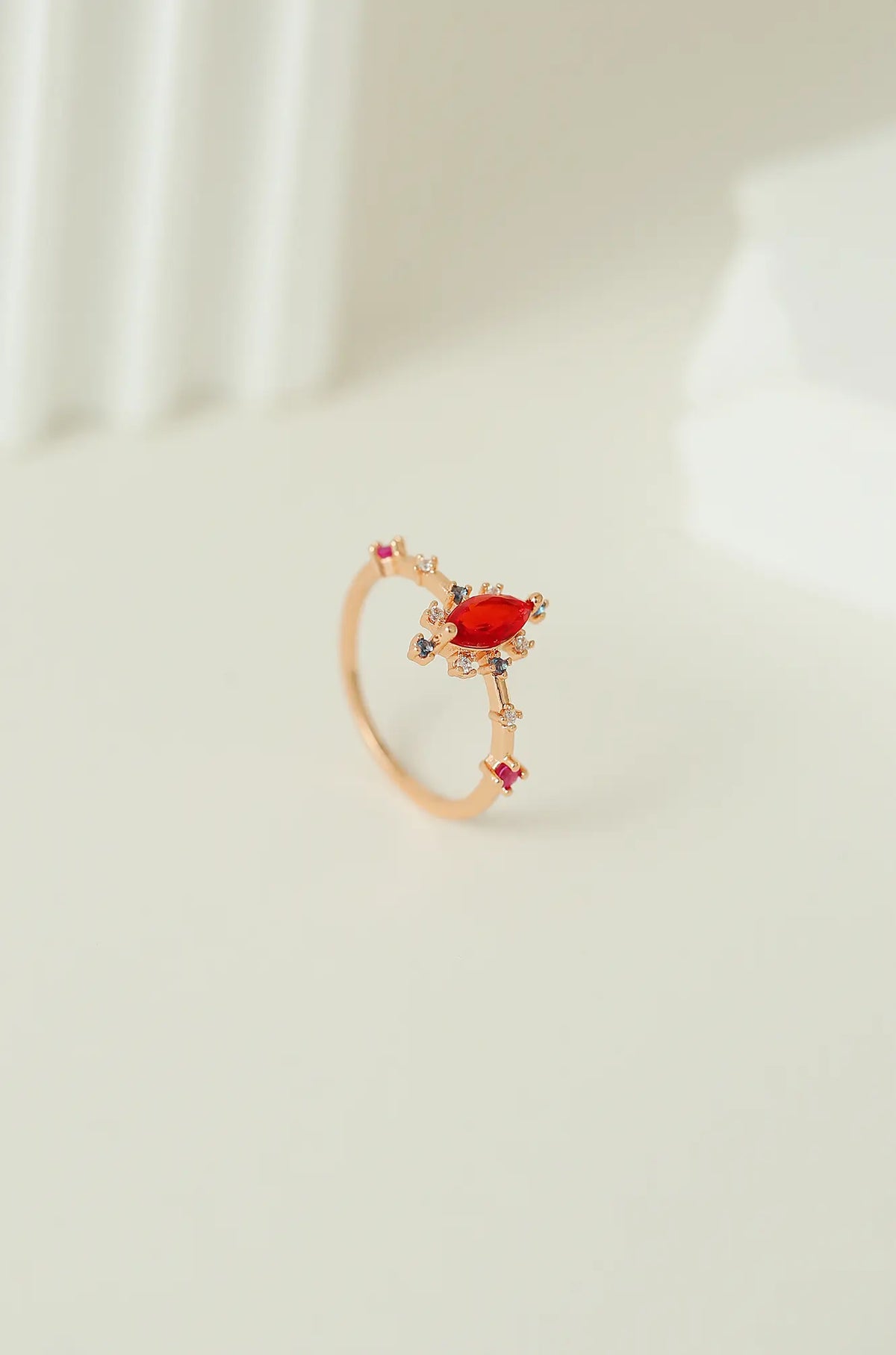 Rose gold ring shown upright, with a red marquise-cut center stone