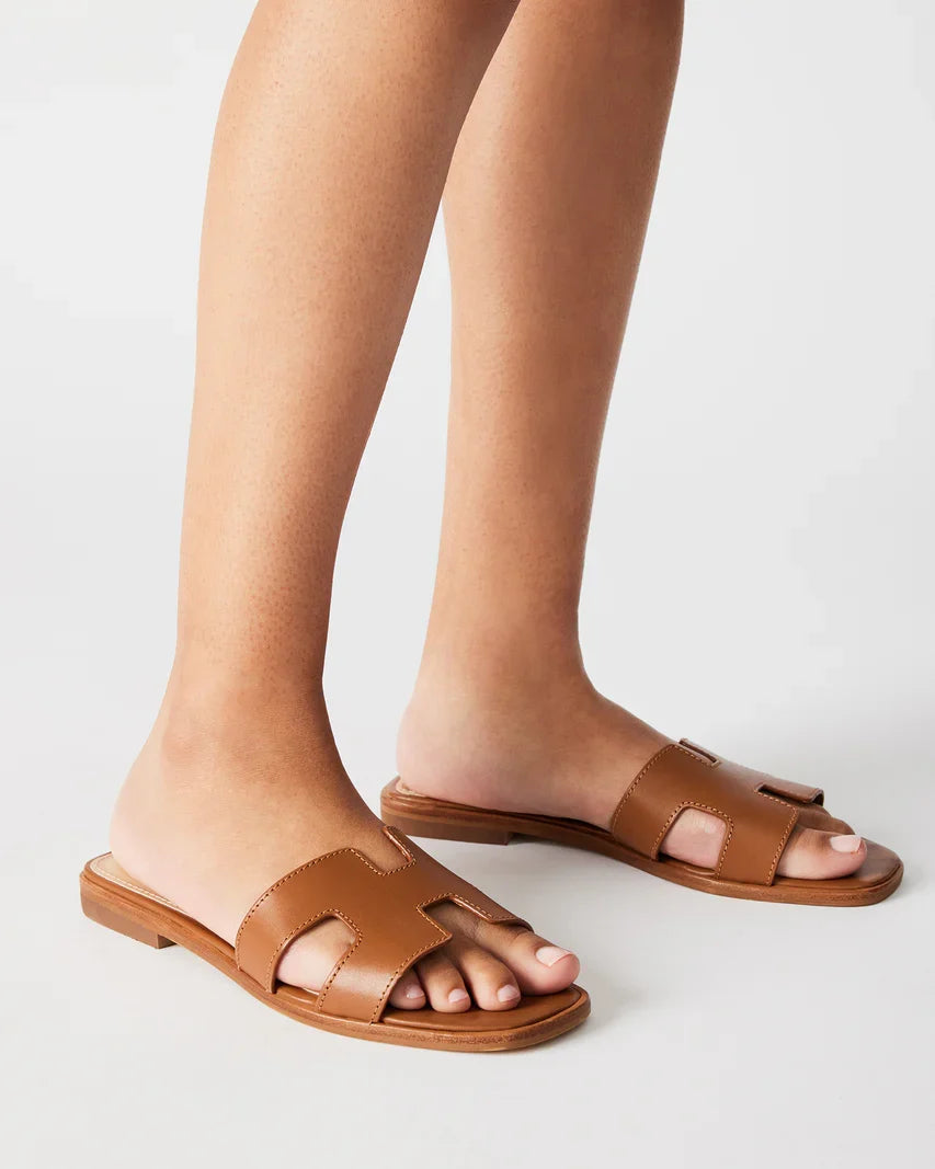 Cognac leather slide sandals on model feet with open toe and flat sole