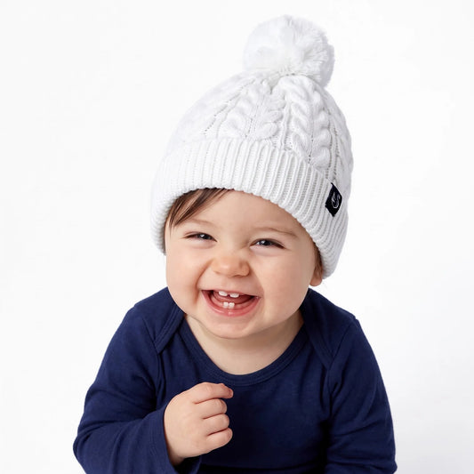 White knit pom beanie on smiling baby, with ribbed cuff and pom-pom.