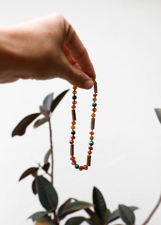 Amber and malachite beaded necklace held in hand, showing dangling beaded strand