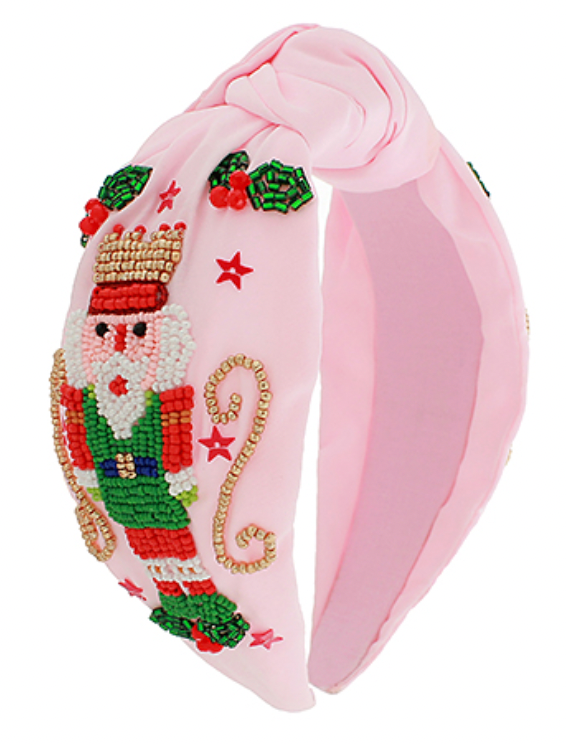 Pink fabric headband with a beaded nutcracker design, stars, and gold-tone scroll details