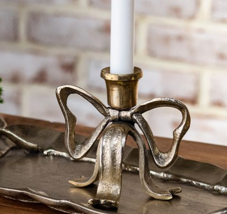 Gold-tone candle holder with a sculptural bow-shaped base and white taper candle