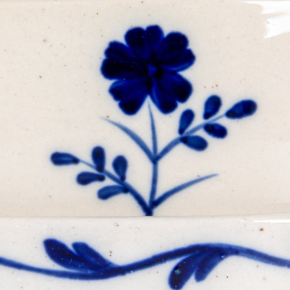 Close-up of hand-painted blue flower on cream ceramic butter dish lid