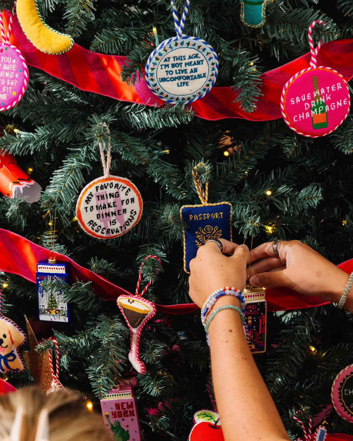 Needlepoint passport icon ornament on a Christmas tree, blue fabric with gold stitched design.