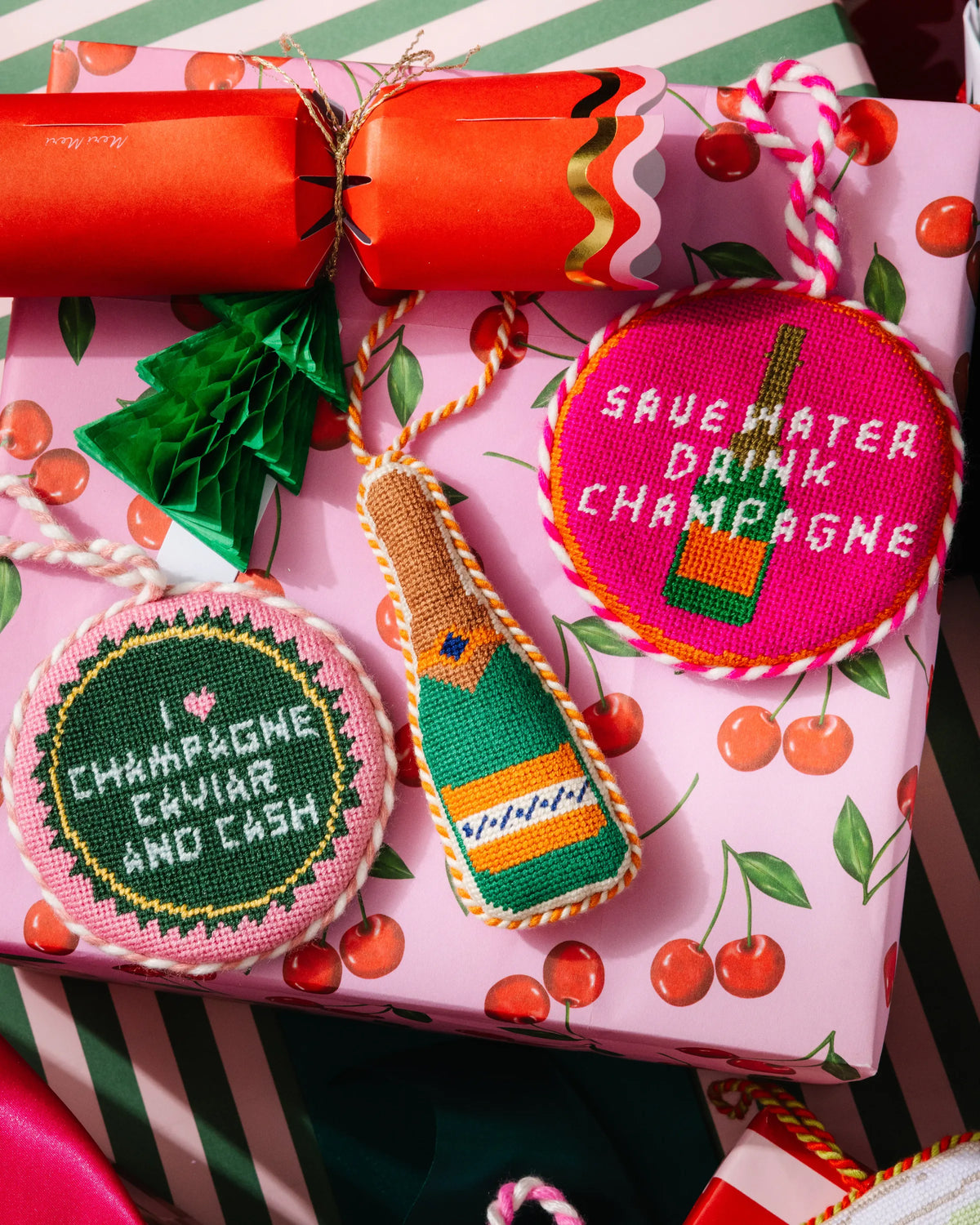 Needlepoint bottle ornament in a gift box, green label and orange top with hanging loop.