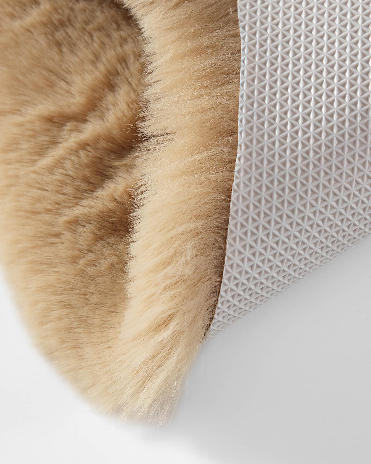 Tan faux fur rug edge with woven textured backing visible