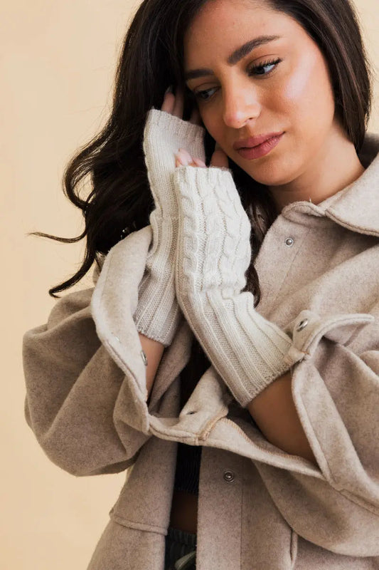 Ivory cable-knit fingerless gloves shown on a model’s hands with open fingers
