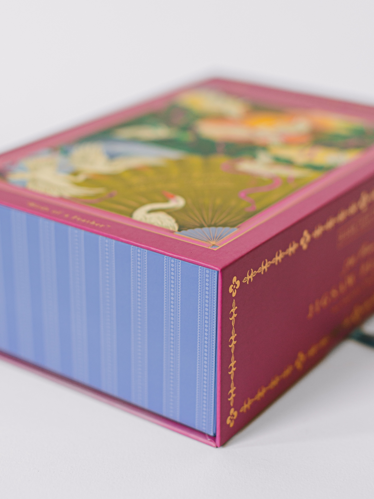 Jigsaw puzzle box corner with blue striped side and pink frame with gold script