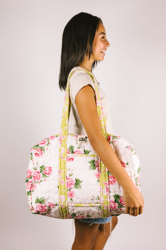 Floral quilted duffle bag in pink roses with yellow-green straps, worn over shoulder
