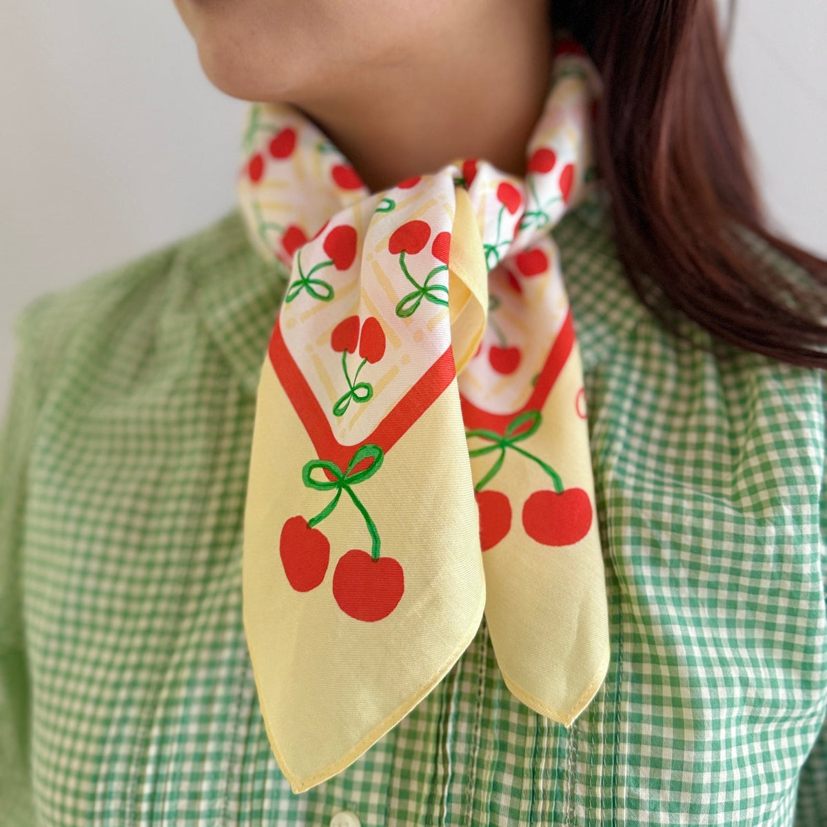 Cherry bandana tied at neck, cream fabric with red cherry pattern and green stems