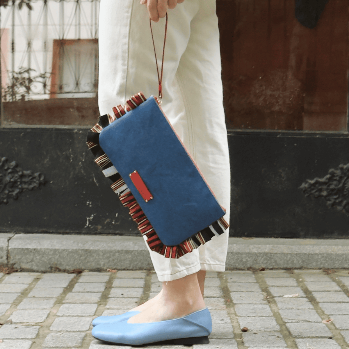 Denim clutch bag with blue front, striped trim edges, and red zipper pull