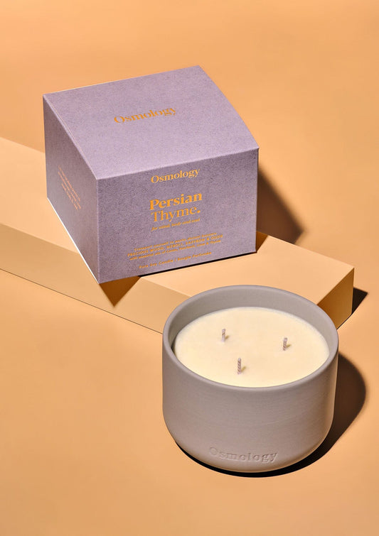 Triple-wick scented candle in a white wax jar, beside purple cube gift box