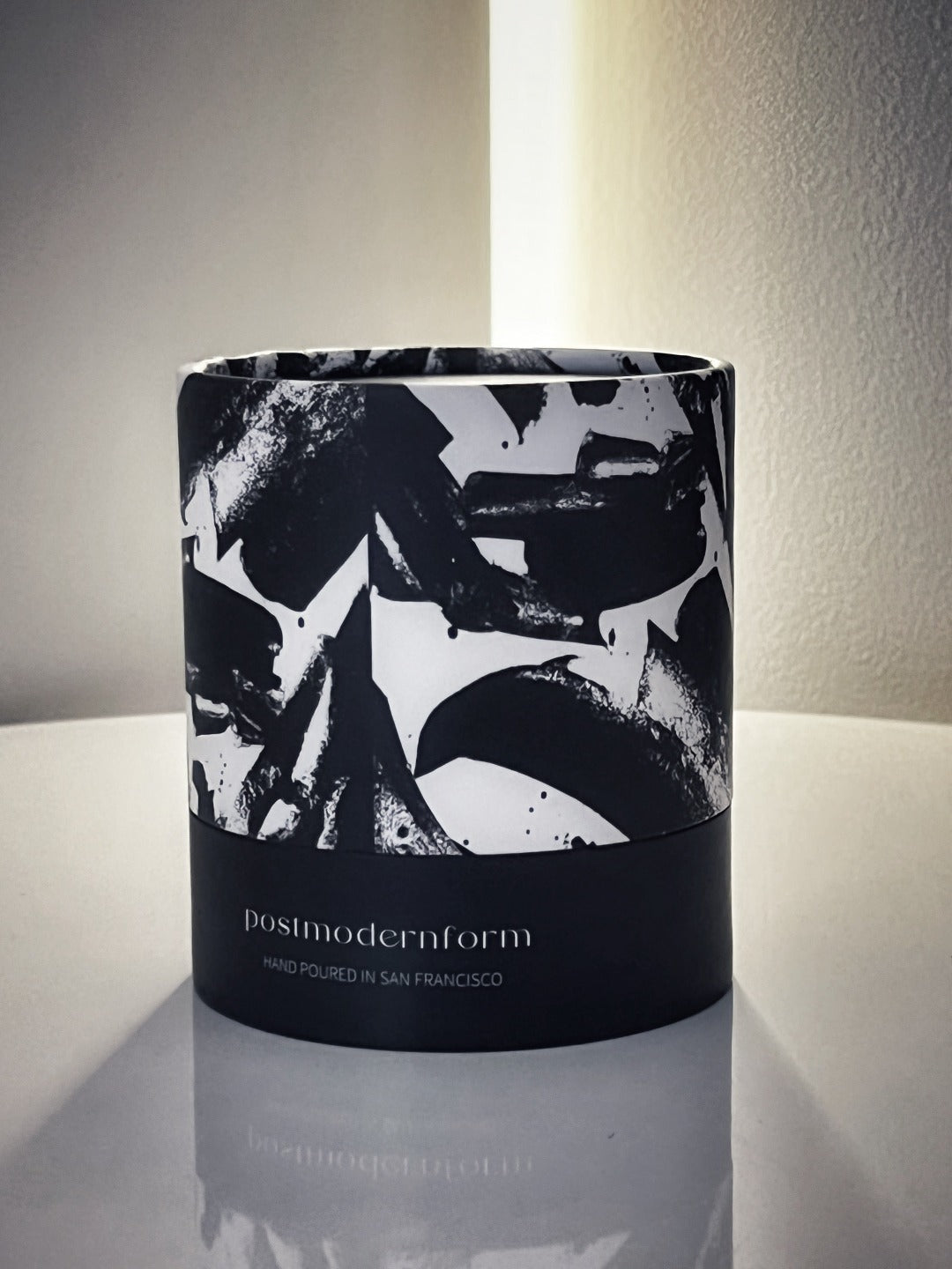 Black patterned candle sleeve with 'posmodernform' text and studio-lit jar candle.