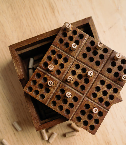 Angled view of carved wooden peg puzzle board with round holes and numbered pegs
