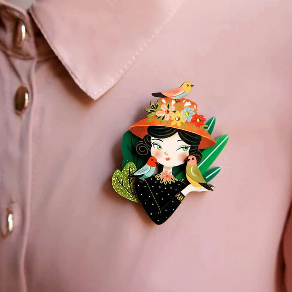 Bird lover brooch pinned on pale pink shirt, illustrated woman with floral hat and birds
