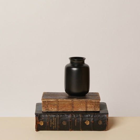 Black vase with wide neck standing on stacked books