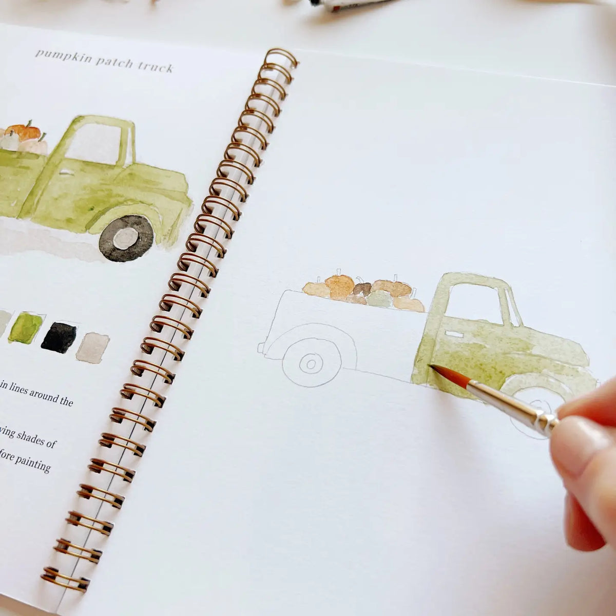 Watercolor workbook page with outlined truck sketch and painted patches, brush in hand