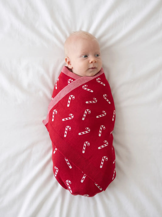 Red knit baby blanket with white candy cane print, swaddled around a baby