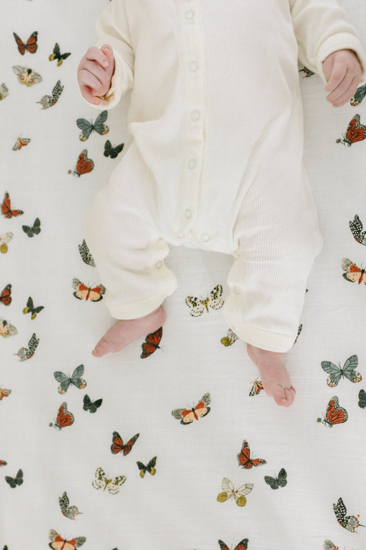 Off-white crib sheet with colorful butterfly pattern, baby feet visible at edge