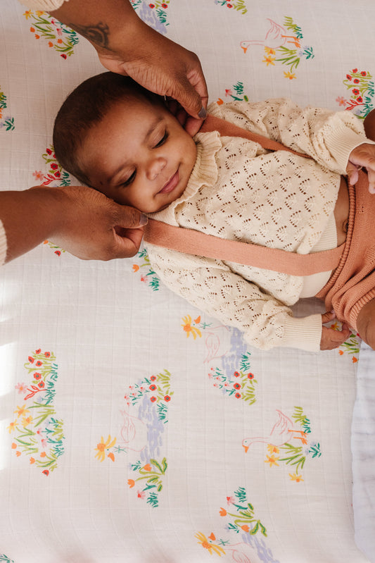 Newborn resting on patterned crib sheet with pastel geese and flowers.