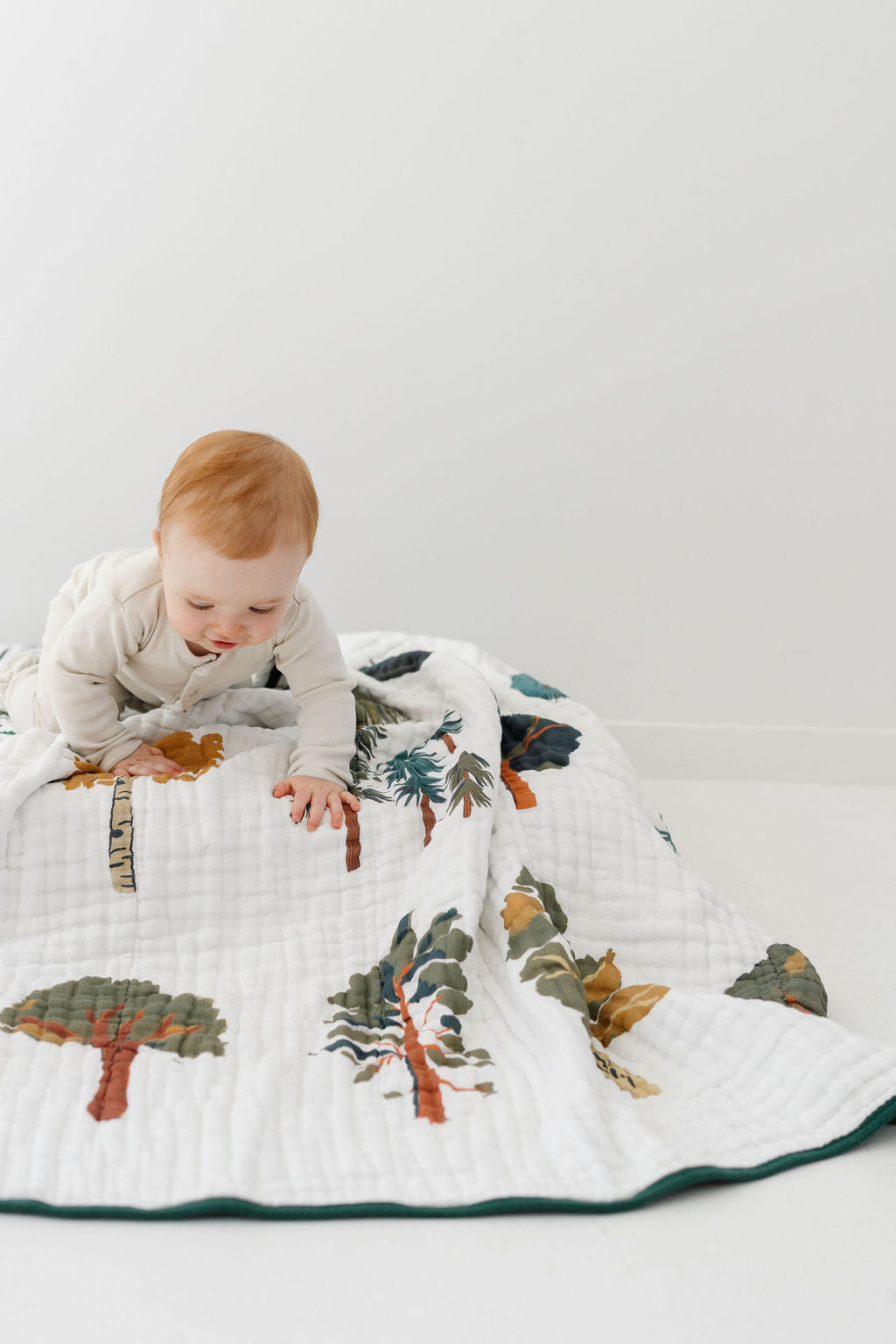Forest trees quilt spread on floor, baby on top of white woodland print