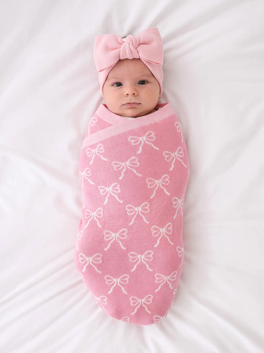 Pink knitted baby swaddle blanket with white bow pattern and matching bow hat.