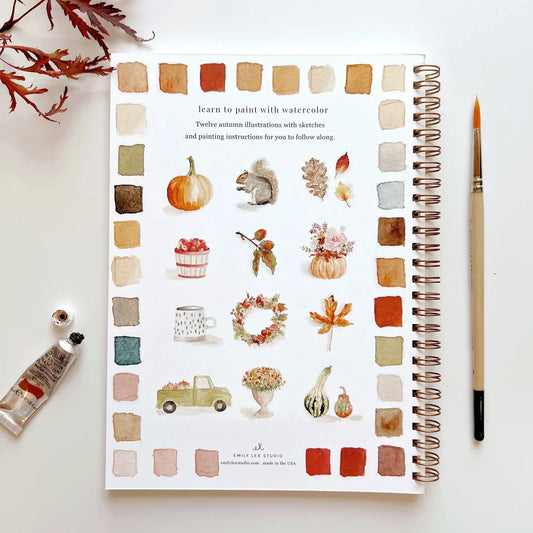 Open watercolor workbook page with autumn examples, paint swatches, and paintbrush