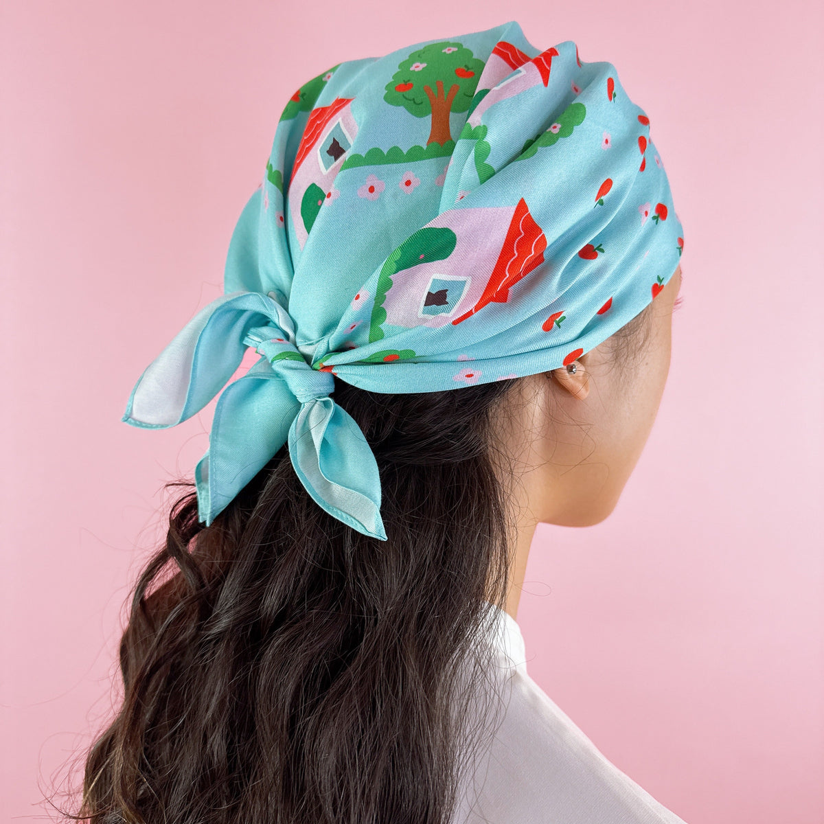 Light blue silk square scarf head tie, with village-and-tree print and red accents.